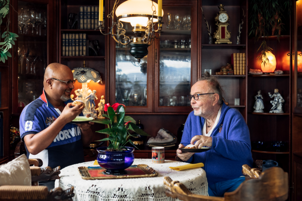 To eldre menn sitter rundt et bord og spiser